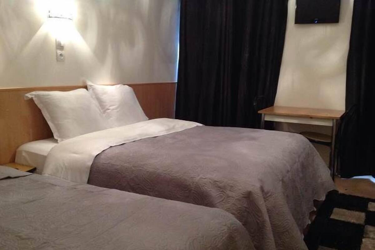 A hotel room with two beds, a nightstand, a lamp, and a TV on the wall.