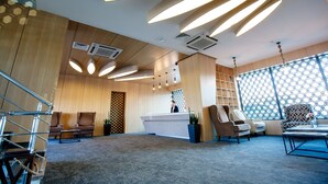 A modern reception area with a wooden reception desk, multiple seating options, and a large window with a geometric pattern. - Cruise Hotel (Tbilisi)