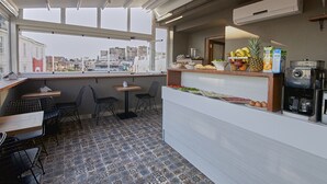 A modern cafe with a tiled floor, a counter with food and drinks, and a view of the city through large windows. - Arart Hotel (Istanbul)