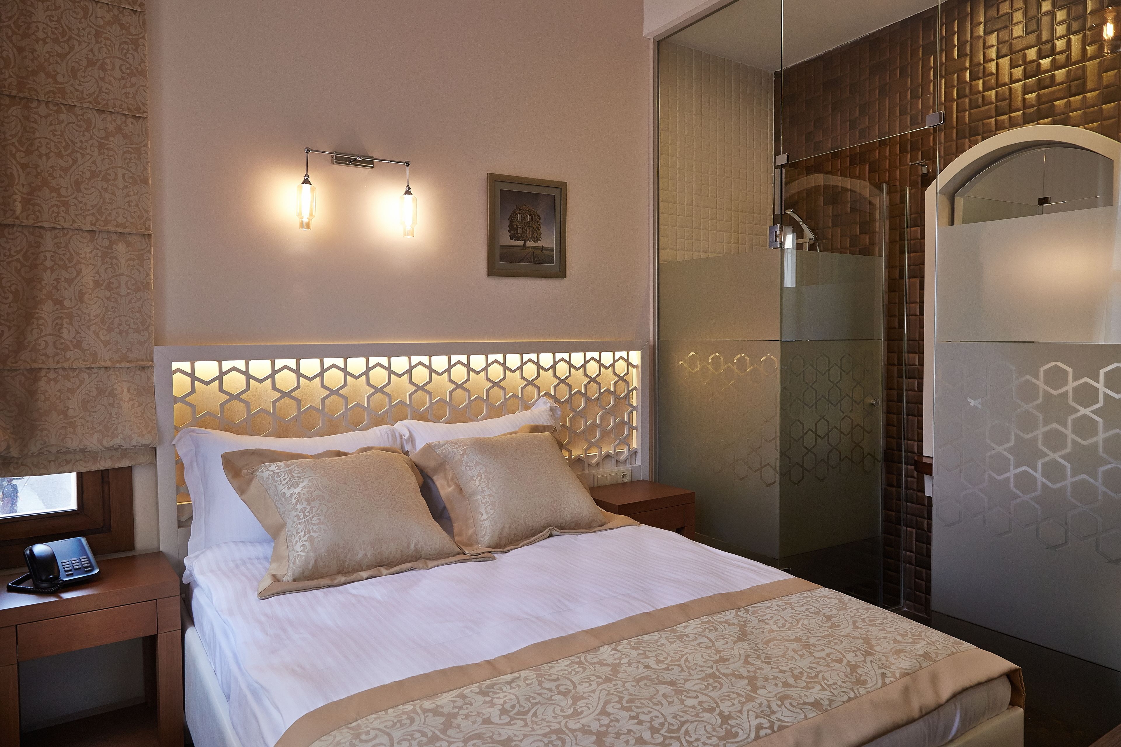A hotel room with a bed, bedside tables, a phone, a picture on the wall, and a shower area.