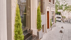 A building with a classic architectural style, featuring a prominent entrance with a glass door and steps leading up to it. There are two potted evergreen trees flanking the entrance, and a street lamp is mounted on the wall to the left. - Arart Hotel (Istanbul)