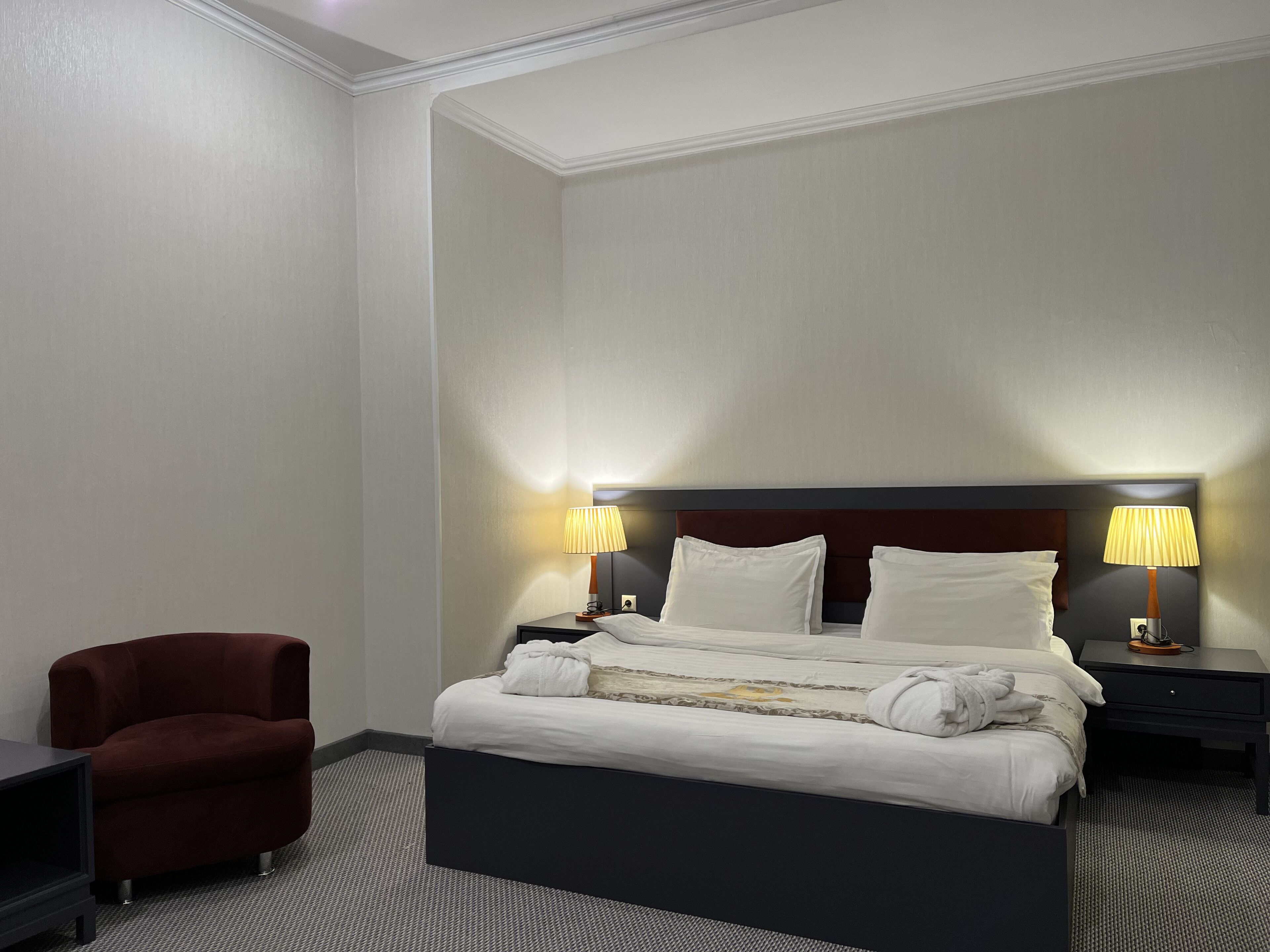A hotel room with a large bed, two bedside lamps, a red armchair, and a small table.