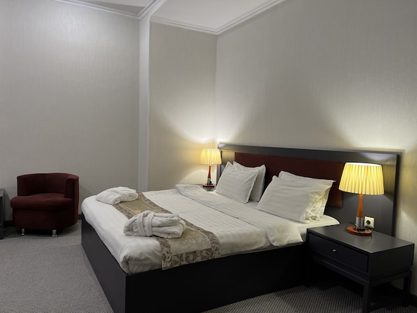 Una habitación de hotel con una cama, dos lámparas de noche, una silla roja y una mesita con lámpara.