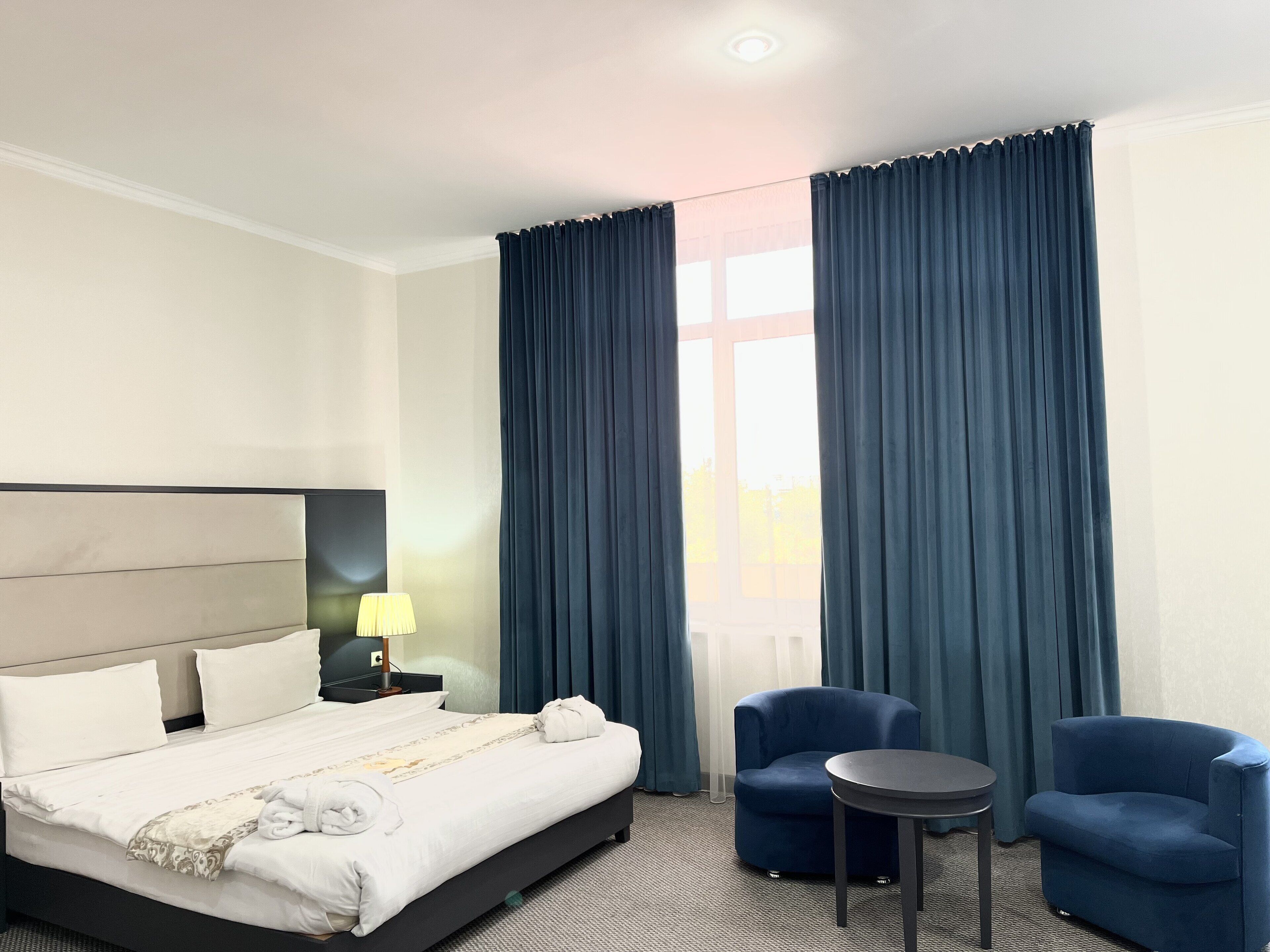Une chambre d’hôtel comprenant un lit, une table de chevet, une lampe, deux fauteuils et une petite table.