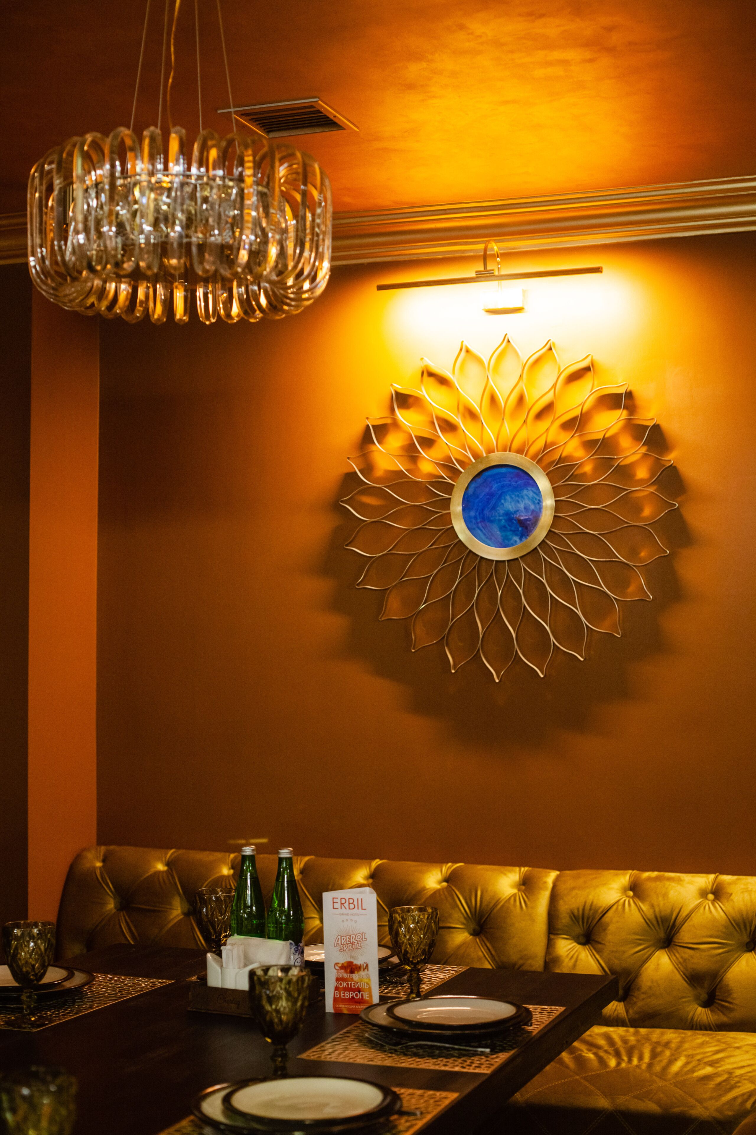 A dining area with a chandelier, a wall-mounted decorative light, and a table set for two with a menu.