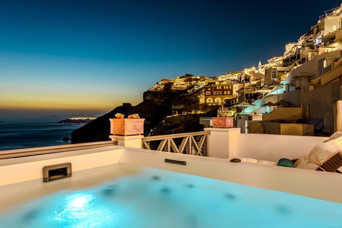 A rooftop pool with a view of a coastal town at night.