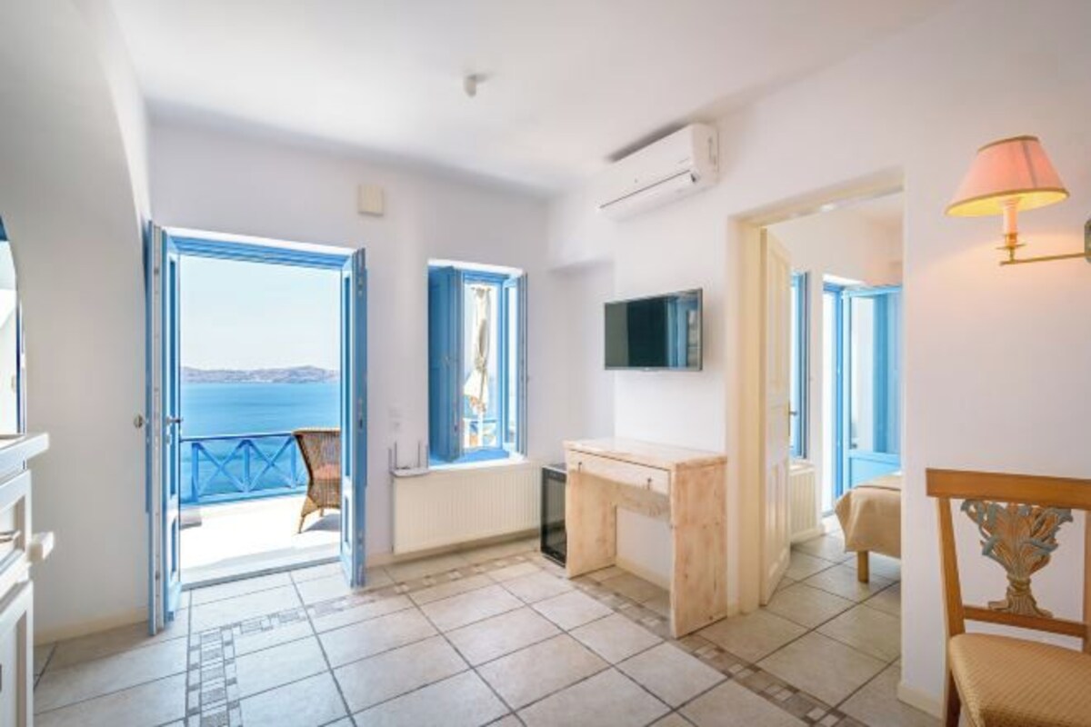 A room with a view of the sea, a desk, a chair, and a bed.