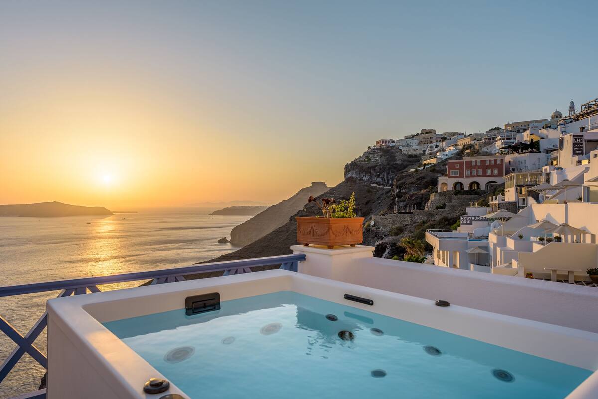 A rooftop pool with a view of the sea and a coastal town at sunset.
