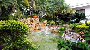 Ein Garten mit Wasserspiel, üppigem Grün und einer Steinmauer.
