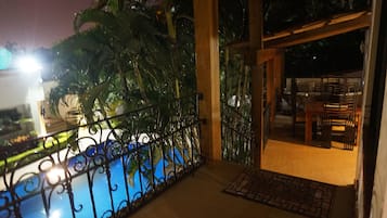 A balcony with a metal railing overlooking a pool and a dining area with chairs and tables.
