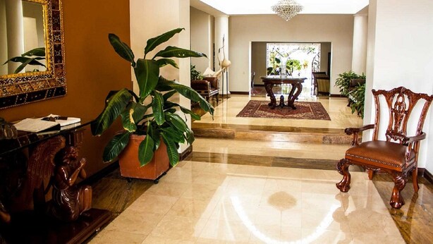 Eine geräumige Lobby mit Marmorboden, einer großen Topfpflanze, einer hölzernen Statue, einem Chandelier und einem Essbereich im Hintergrund.