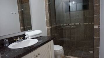 A bathroom with a glass-enclosed shower, a white sink, and a toilet.
