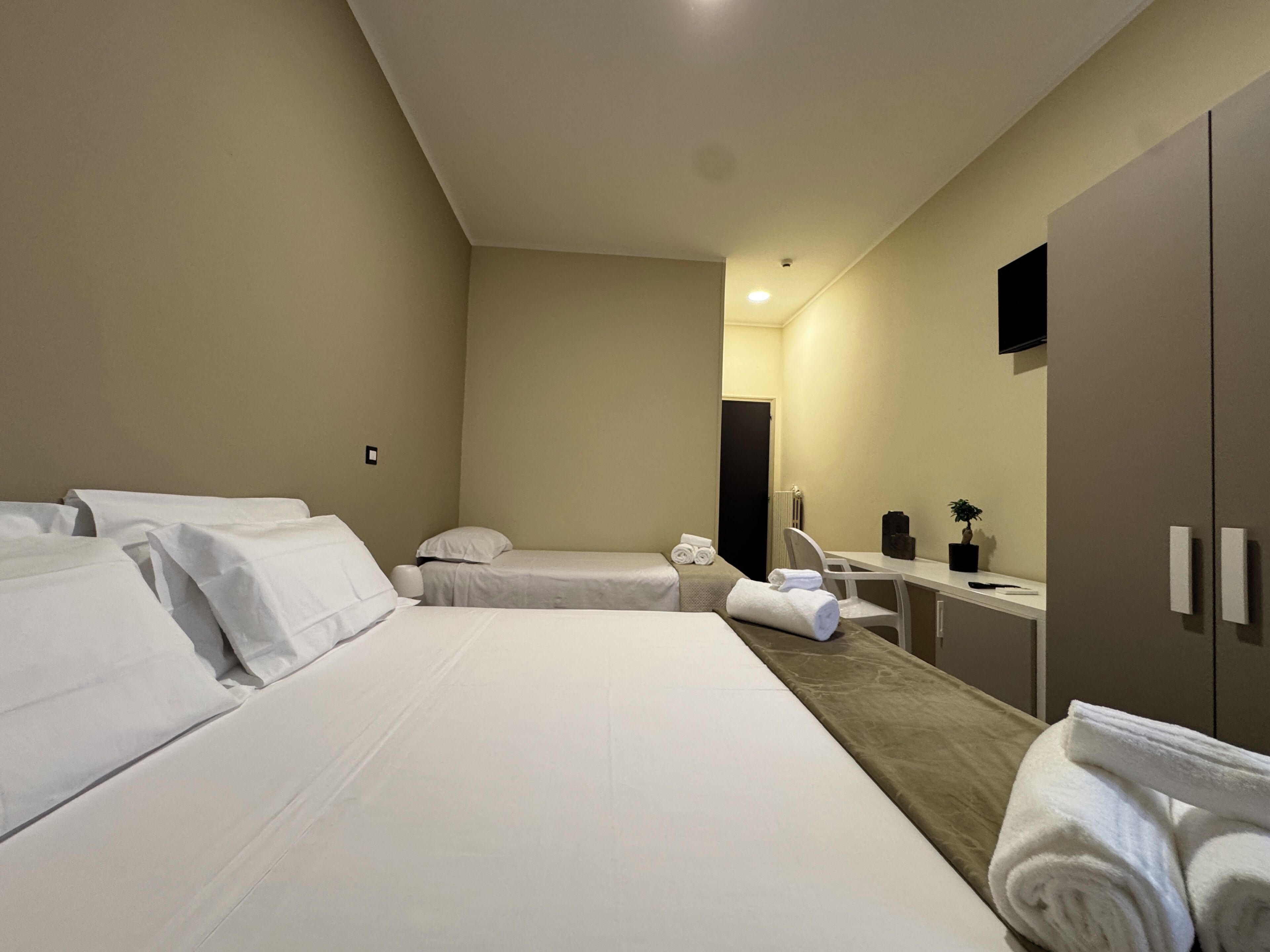 A hotel room with two beds, a desk, a chair, a mirror, a radiator, and a TV on the wall.