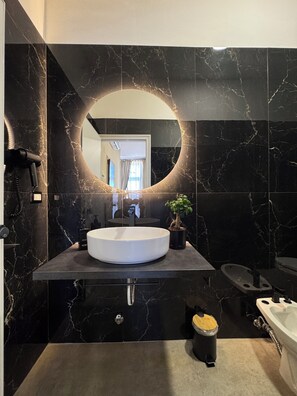 A modern bathroom with a large oval sink, a round mirror, and a potted plant. - Hotel Santuario Pompei (Pompei)