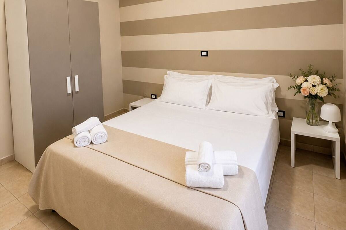A hotel room with a bed, a wardrobe, a nightstand, and a vase of flowers.