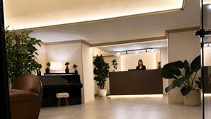 Una zona de recepción con recepcionista, un piano y plantas en macetas.
