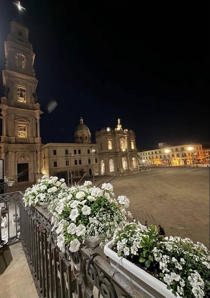 A nighttime view of a plaza with a prominent clock tower and classical architecture.