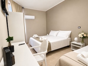 A hotel room with a bed, a desk, a chair, a small table, a plant, and a vase with flowers. - Hotel Santuario Pompei (Pompei)