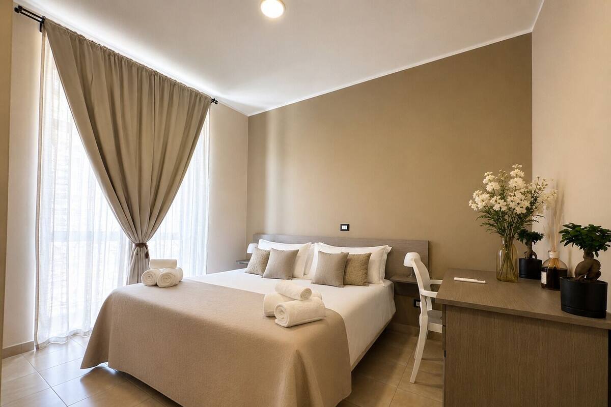 A hotel room with a bed, a desk, a chair, and a window with curtains.