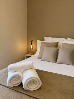 Cama bem arrumada com toalhas brancas dobradas, abajur e mesa de cabeceira.