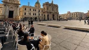 Una plaza con mobiliario exterior, una destacada torre del reloj y arquitectura clásica.
