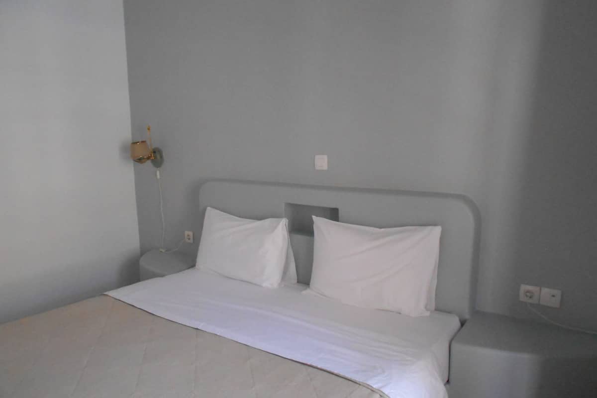 A simple, unadorned bedroom with a single bed, two white pillows, and a plain headboard.