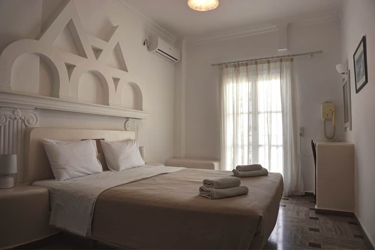 A neatly arranged hotel room with a large bed, a bedside table, a lamp, and a wall-mounted air conditioner.