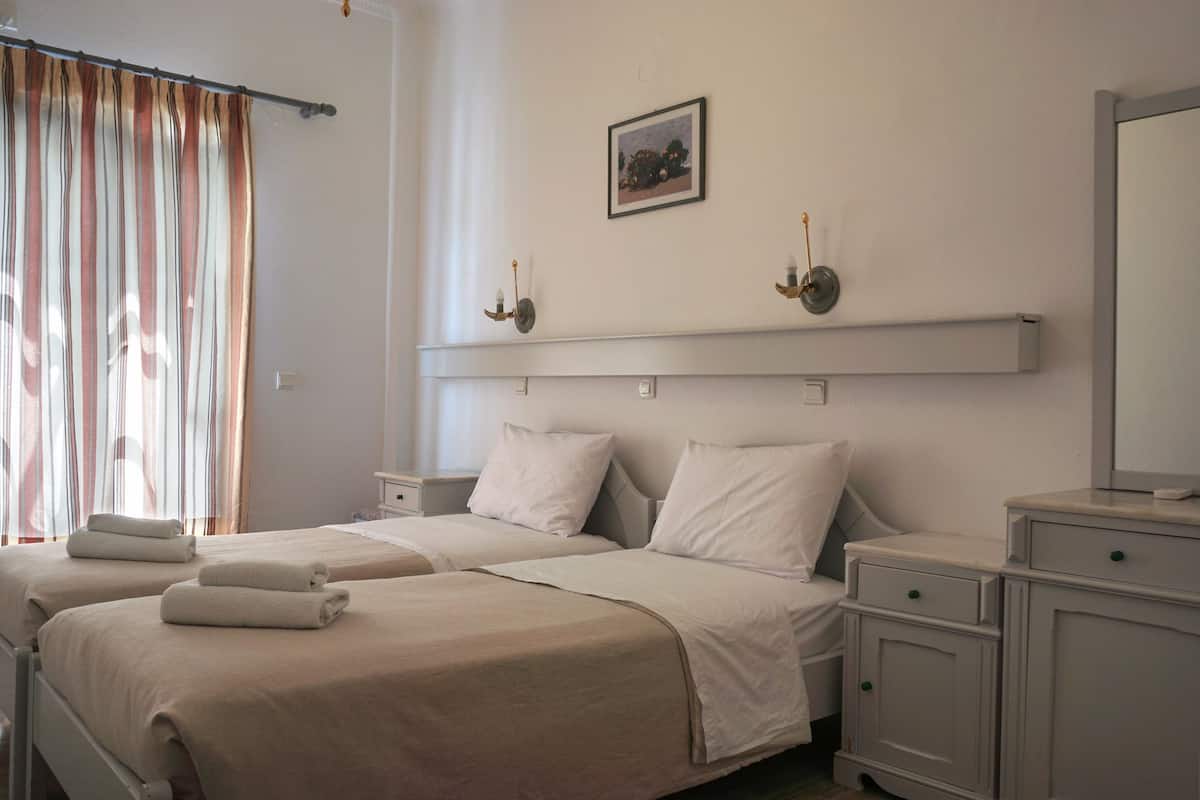 A hotel room with two beds, a bedside table, a nightstand, a mirror, and a picture on the wall.