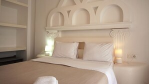 Ein ordentlich gemachtes Bett mit weißem Kopfteil und zwei Kissen, ein Nachttisch mit Lampe sowie eine Wand mit dekorativer Stuckleiste.