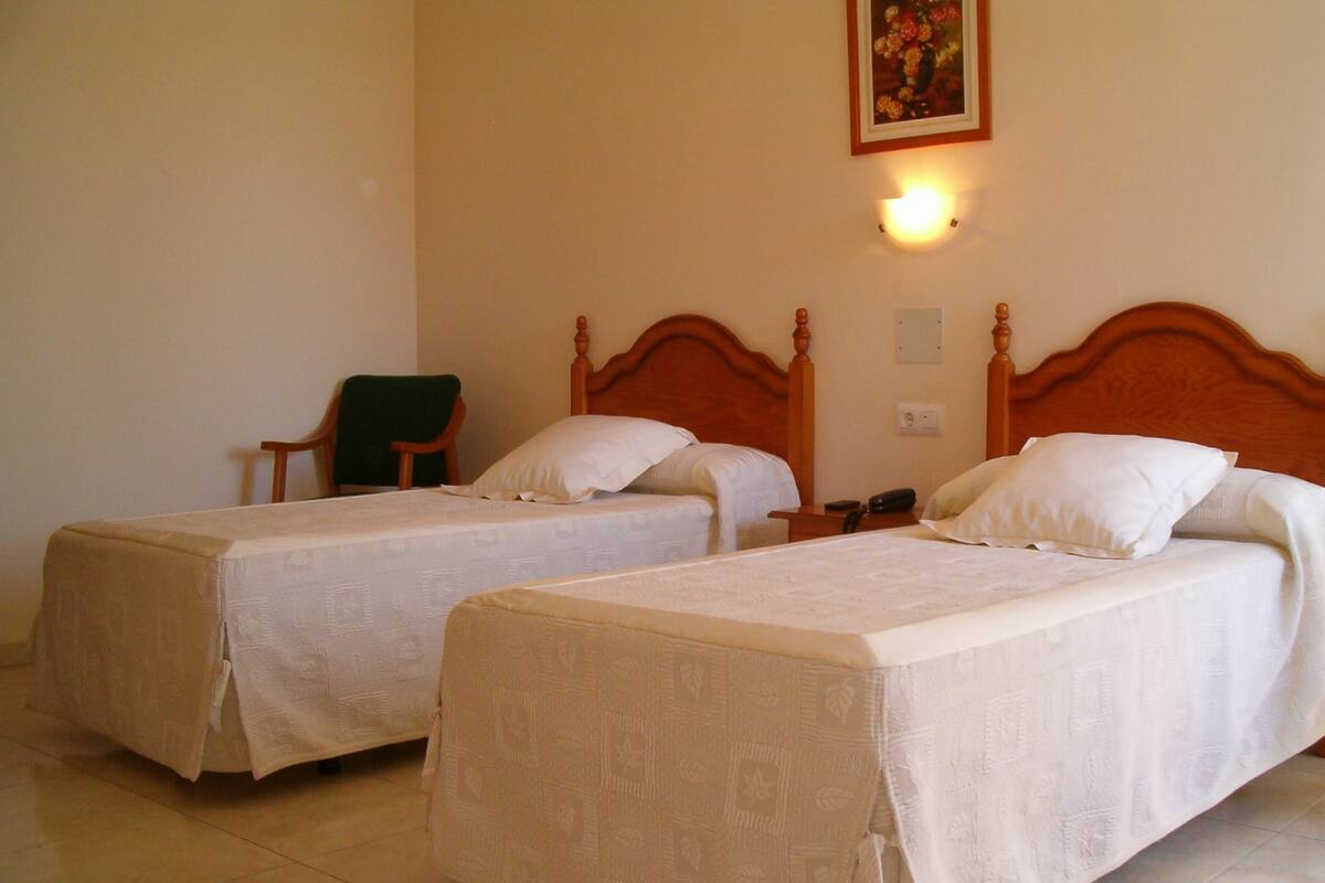 Two single beds with wooden headboards, a green chair, and a wall-mounted light fixture.