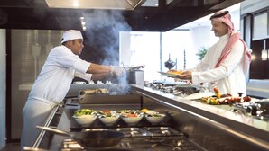 A modern kitchen with chefs preparing food, a stainless steel counter, and a view of the outdoors. - Centro Shaheen Jeddah by Rotana (Jeddah)