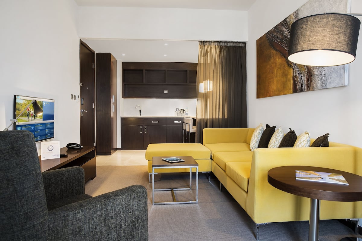 Un salon moderne avec un canapé jaune, un fauteuil gris, une petite table basse et un téléviseur à écran plat posé sur un bureau.