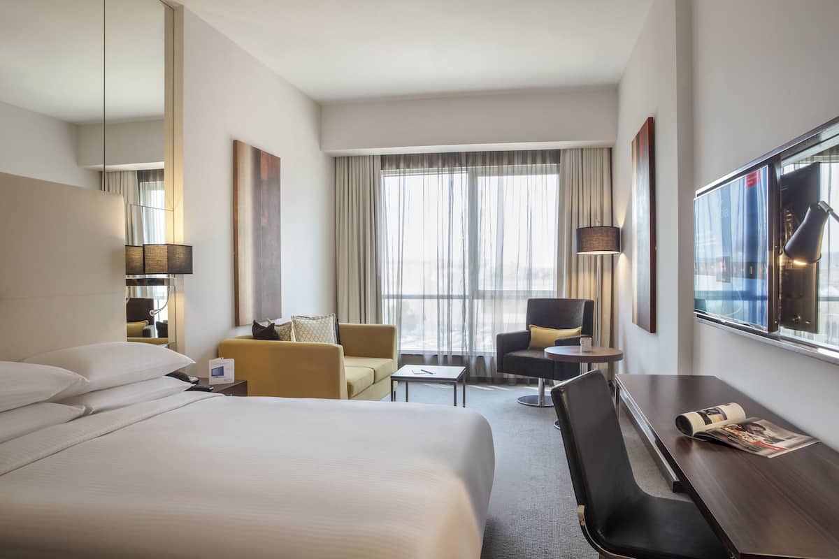 Une chambre d’hôtel avec un grand lit, un bureau, une chaise, un canapé et une fenêtre avec des rideaux.
