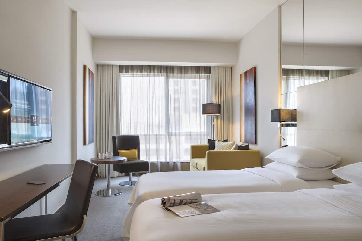 Une chambre d’hôtel avec deux lits, un bureau, une chaise, une petite table et un téléviseur.
