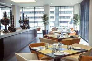 A modern dining area with tables set for two, featuring dark wood tables and beige chairs. - Centro Shaheen Jeddah by Rotana (Jeddah)