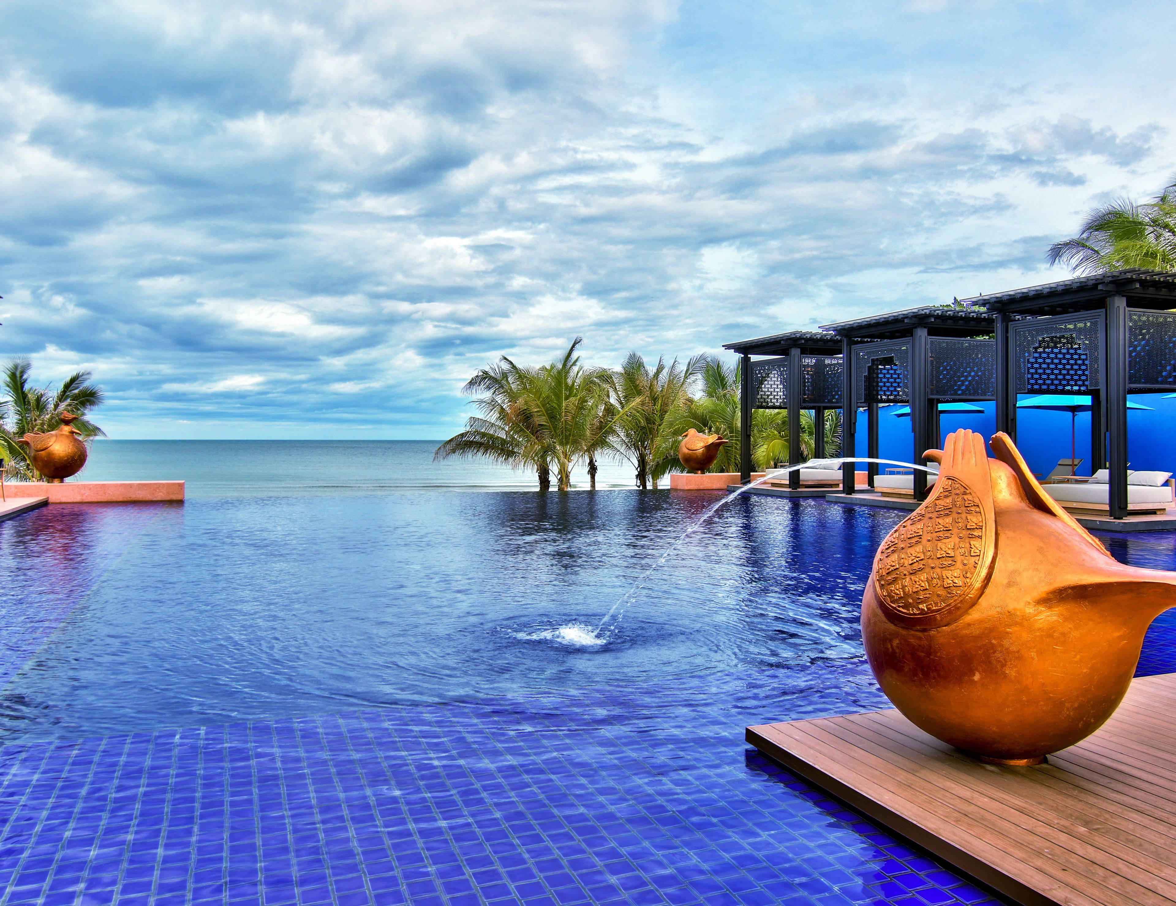 Una piscina infinita con vista al océano, palmeras y un pabellón.