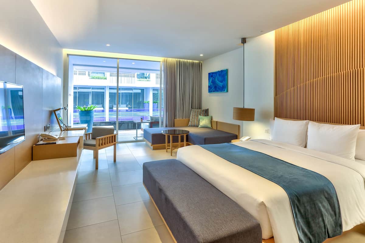 Ein modernes Hotelzimmer mit einem großen Bett, einer Sitzecke mit Tisch und Blick ins Freie.