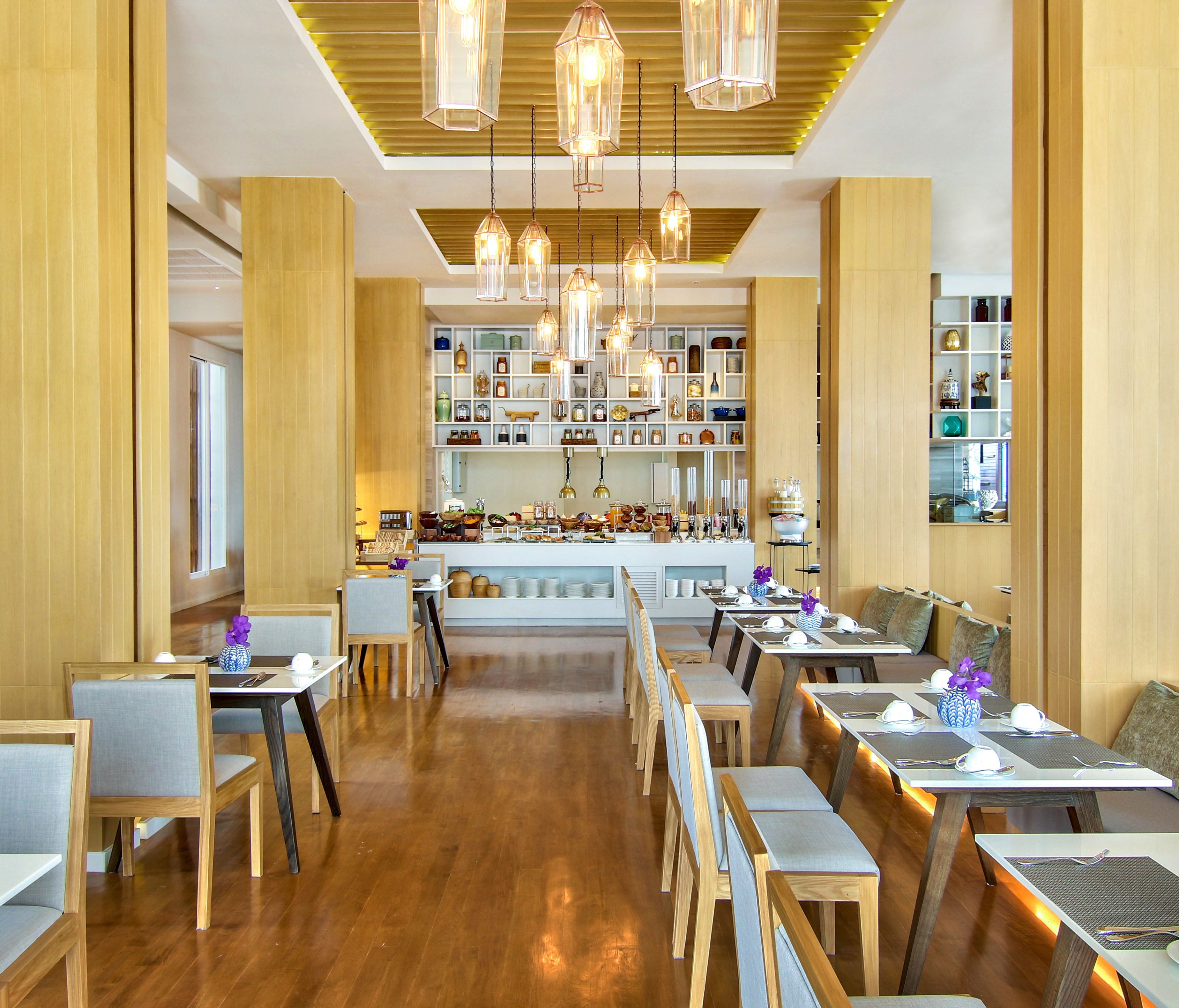 A restaurant with wooden floors, tables, and chairs, and a central counter with various items displayed.