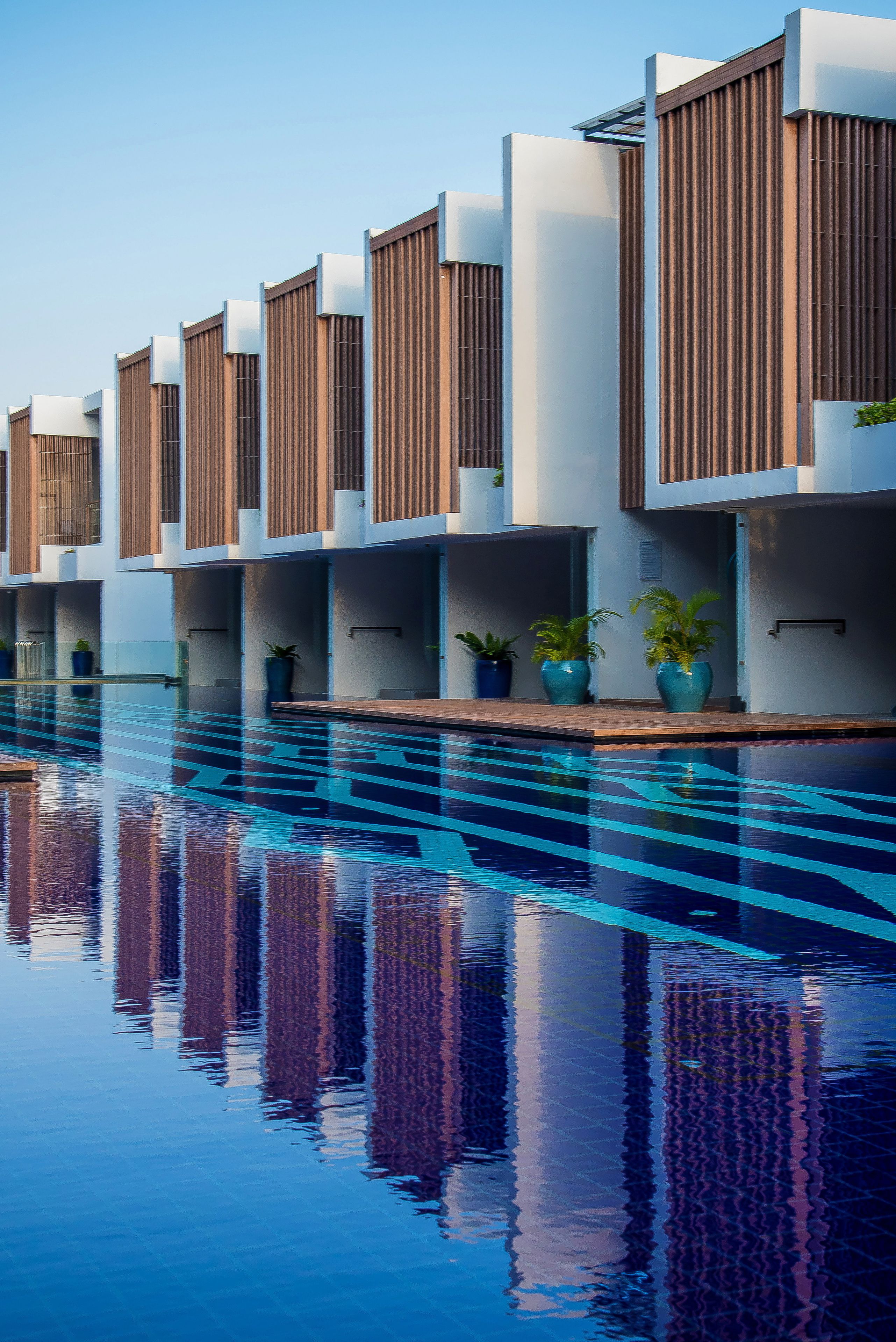 Un hotel moderno con piscina, que cuenta con varias habitaciones con listones de madera y plantas en macetas.