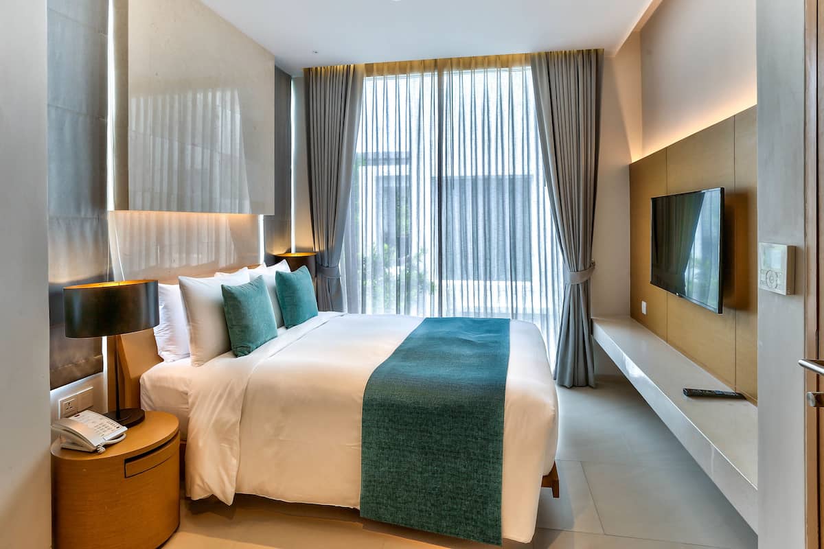 Ein Hotelzimmer mit einem großen Bett, einem an der Wand montierten Fernseher und einem Nachttisch mit Lampe und Telefon.
