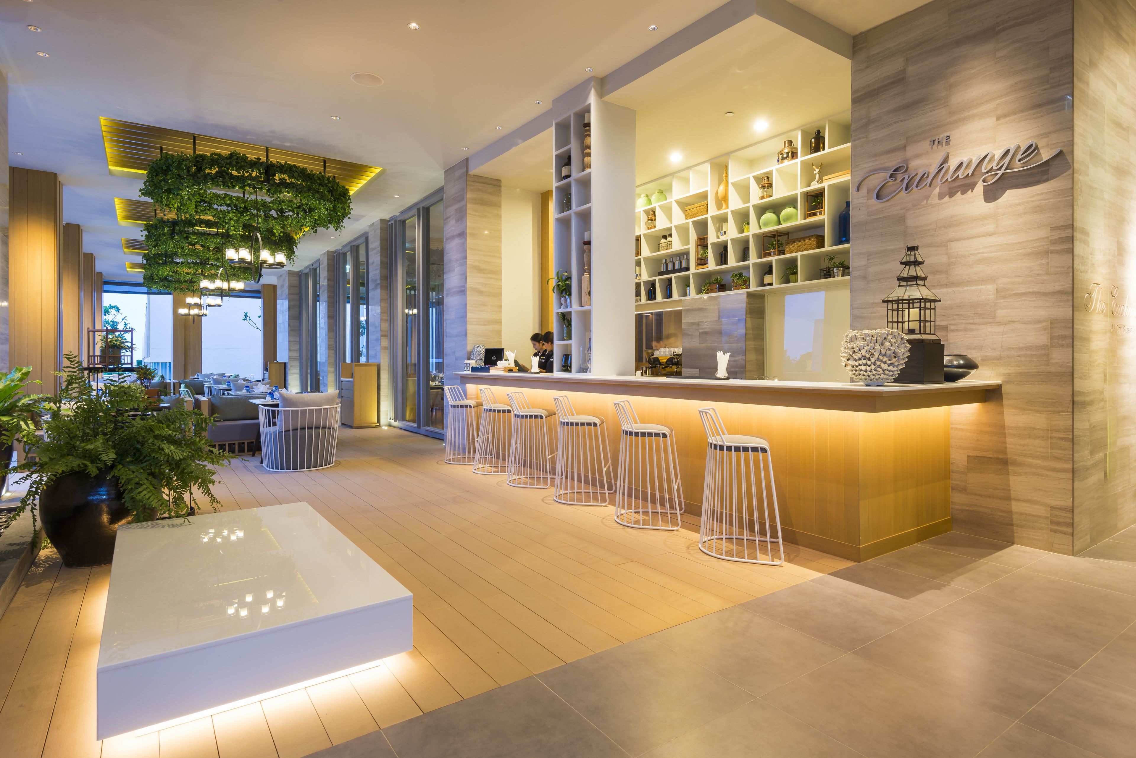 A modern bar area with a wooden counter, bar stools, and shelves with bottles.