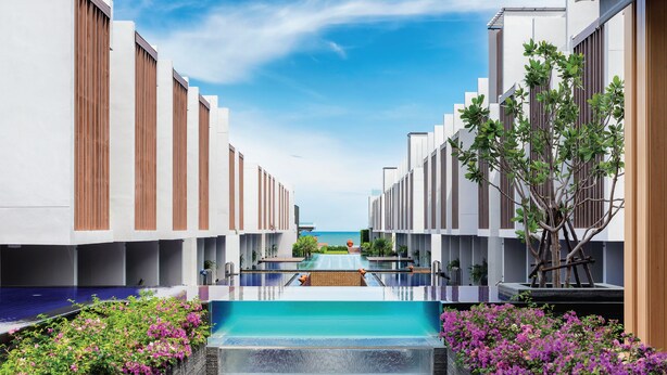A modern hotel with a central pool, surrounded by lush greenery and a clear view of the sea.