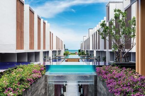 Un hôtel moderne doté d’une piscine centrale, entouré d’une végétation luxuriante et offrant une vue dégagée sur la mer.