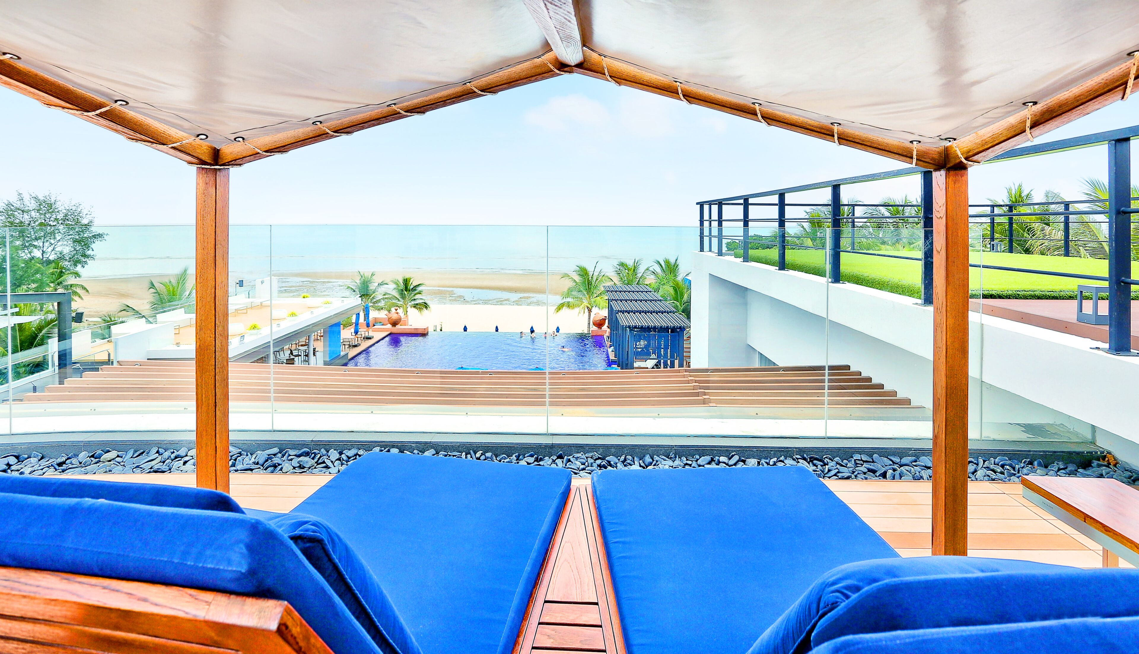 Un espace aménagé au bord de la piscine, avec des chaises longues, une vue sur la plage et un escalier menant à une terrasse.