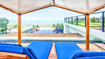 A poolside area with lounge chairs, a view of the beach, and a staircase leading to a deck.