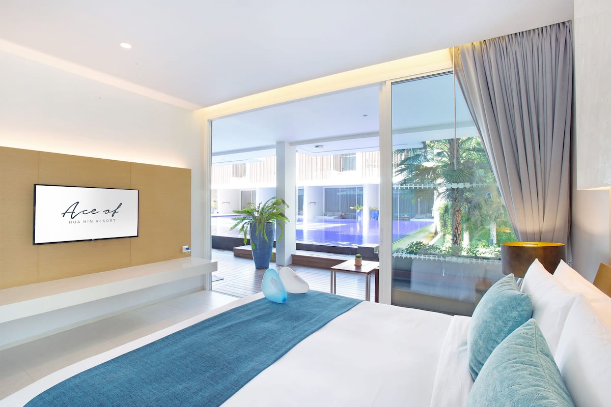 Ein modernes Hotelzimmer mit einem großen Bett, Blick auf einen Swimmingpool und einem gerahmten Schild an der Wand.