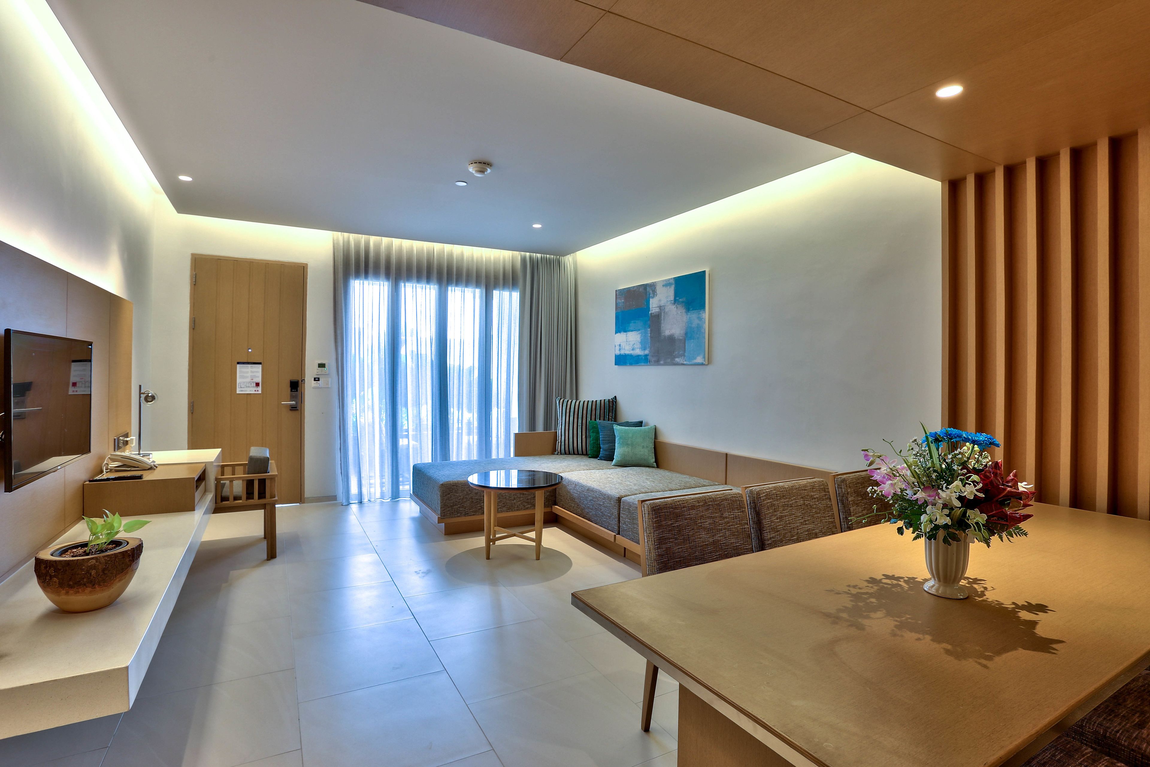 Una habitación de hotel moderna con un sofá, una mesa de comedor, un televisor y una planta en maceta.