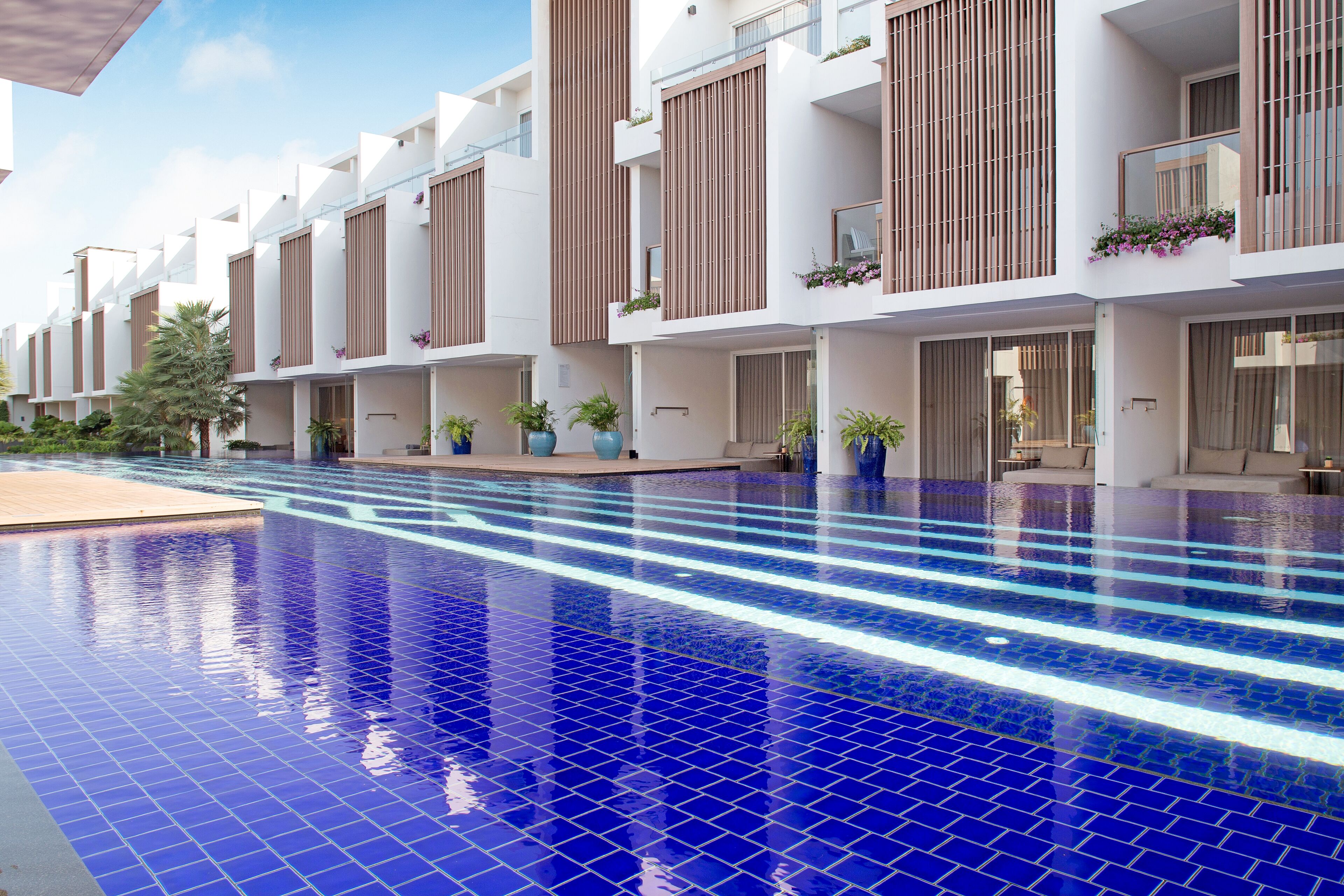 Un hotel moderno con piscina, balconi fioriti e un solarium piastrellato pulito.