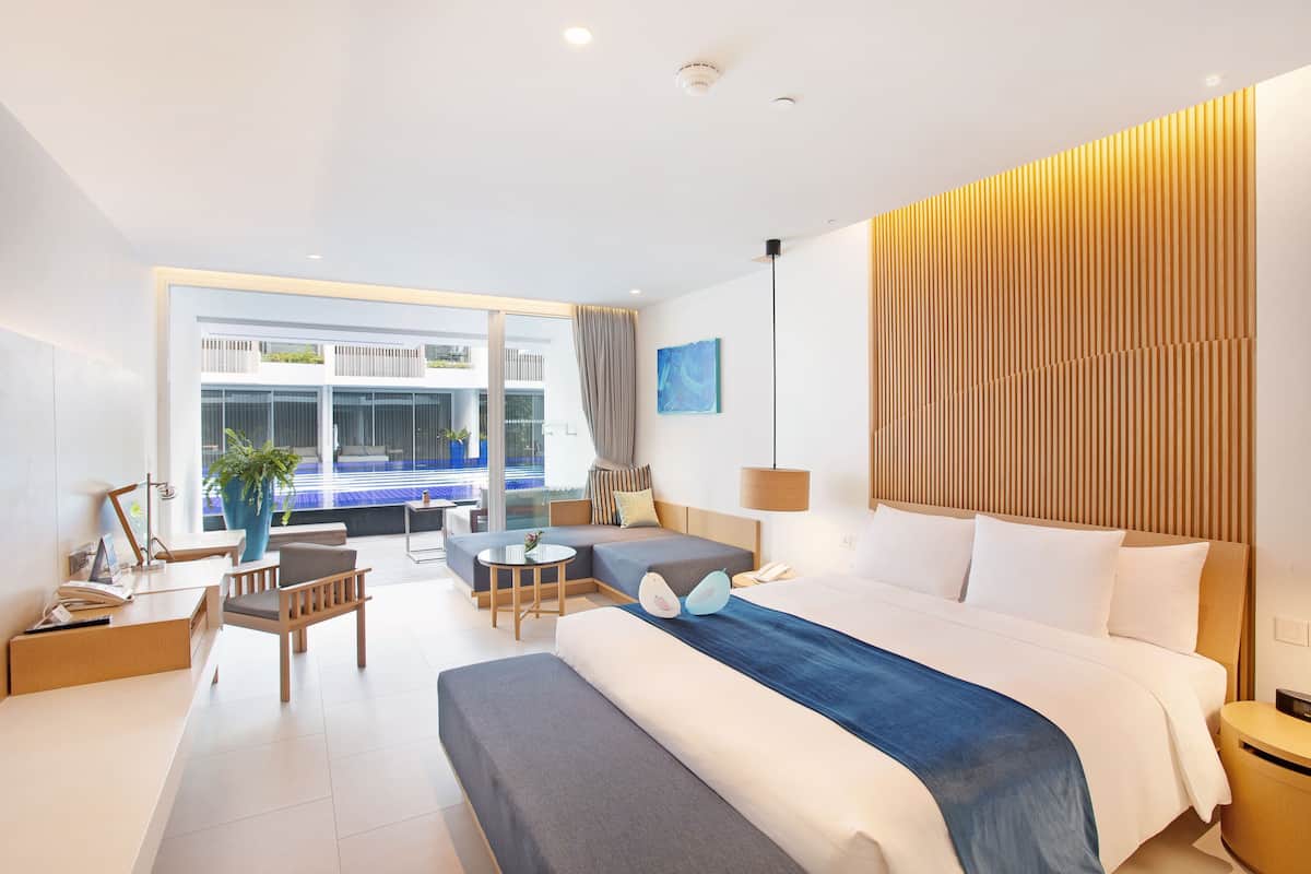 Ein modernes Hotelzimmer mit einem großen Bett, einem Schreibtisch, einer Couch und Blick auf einen Pool.