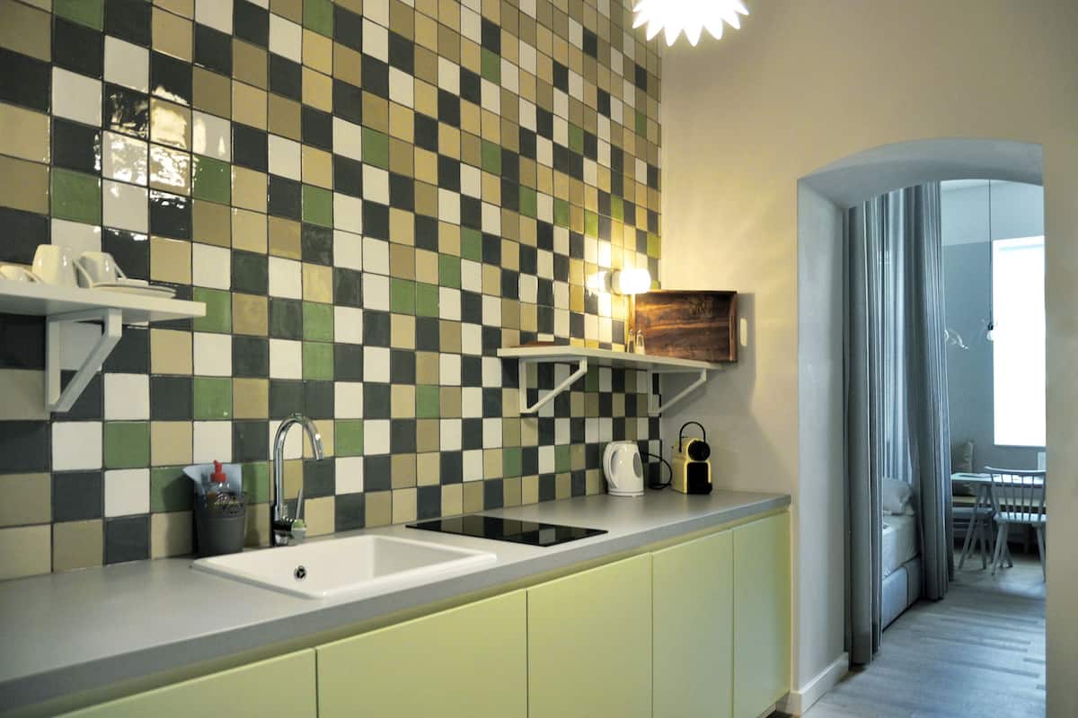 A kitchen with a checkered backsplash, a sink, and a countertop with a kettle and a coffee maker.